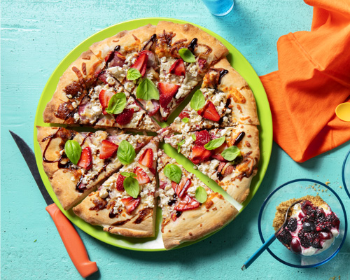 Strawberry Margherita pizza sliced and set on top of a bright green plate, over a blue counter top. 