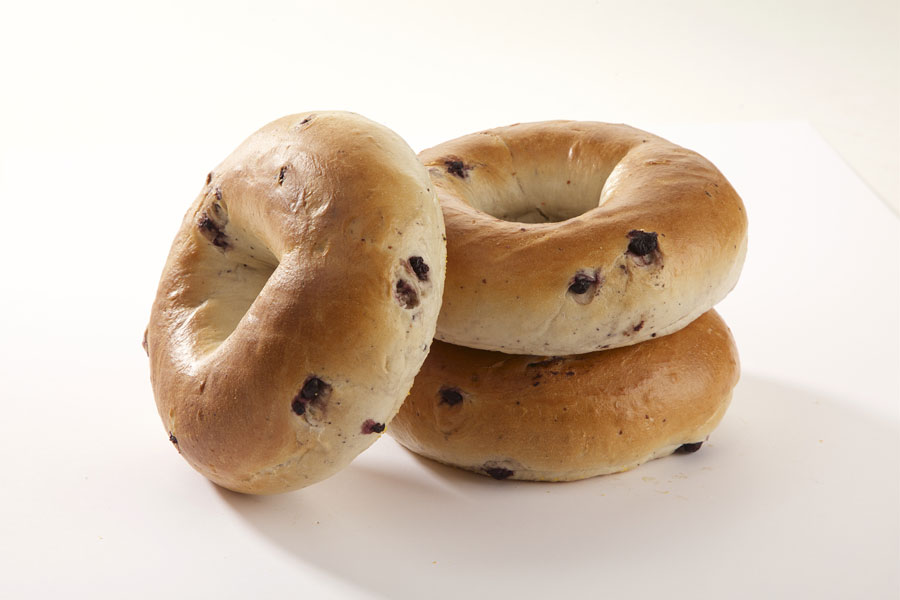 Three blueberry bagels, two stacked on top of each other with one leaning against it on a white board.