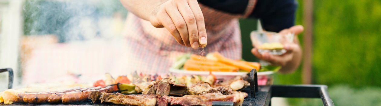 Man seasoning his BBQ food on top of the grill with a little salt.