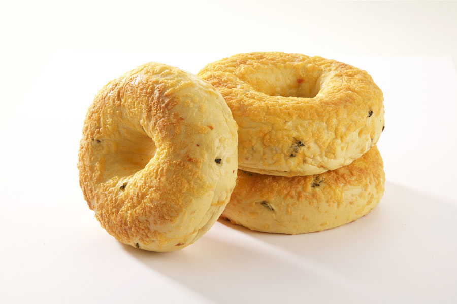 Three jalapeno cheese bagels, two stacked on top of each other with one leaning against it on a white board.