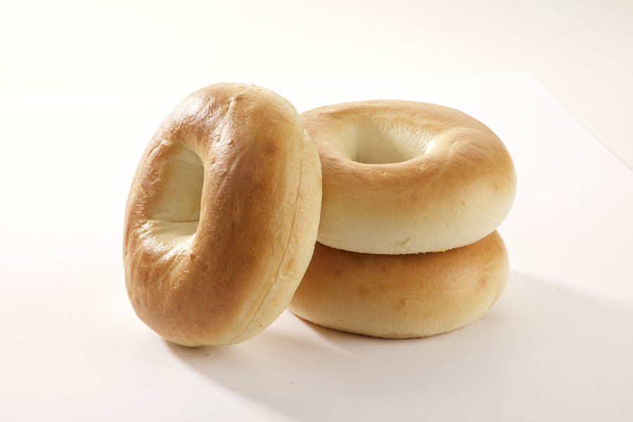 Three plain bagels, two stacked on top of each other with one leaning against it on a white board.