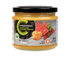 Clear glass jar of Compliments plant-based queso dip pictured was a dip on red tortilla chips on the jar.