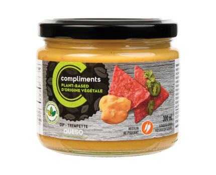 Clear glass jar of Compliments plant-based queso dip pictured was a dip on red tortilla chips on the jar.