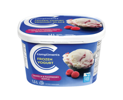 Blue tub of Compliments Vanilla & Raspberry Ripple Frozen Yogurt with a scoop on the front beside two fresh raspberries.