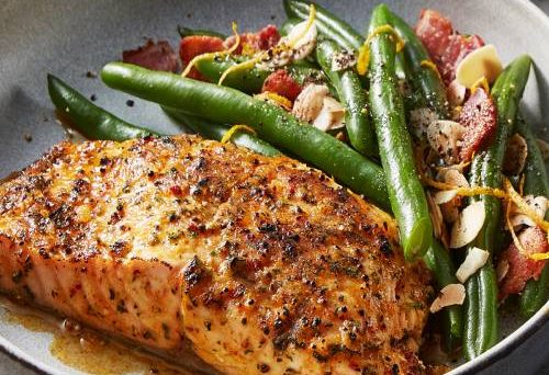 A cooked fillet of salmon in a grey bowl next to cooked vegetables.