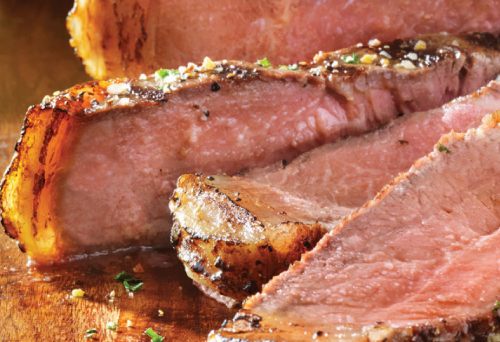 Slices of spiced strip loin steak presented on a cutting board with a steak knife.