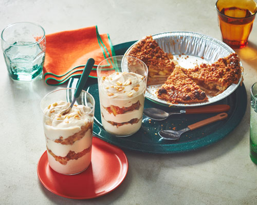 Apple crumble pie next to tall glassed layered with the pie, vanilla yogurt and peanutbutter.