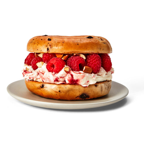 Blueberry bagel topped with cream cheese, yogurt, raspberry jam, fresh raspberries and almonds.