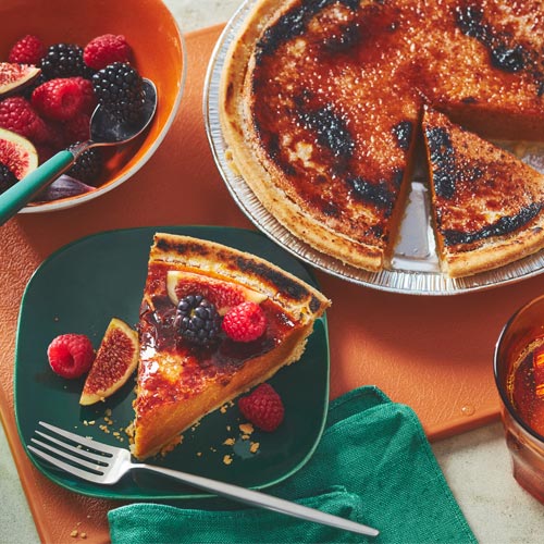 Bruleed pumpkin pie sitting next to a slice garnished with fresh figs, blackberries and raspberries.