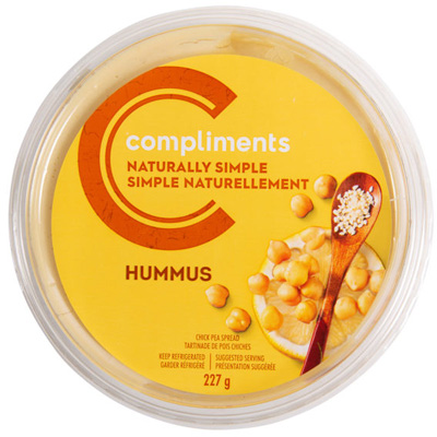 A plastic container of Compliments Naturally Simple Traditional Hummus with a yellow and orange sticker on the front.