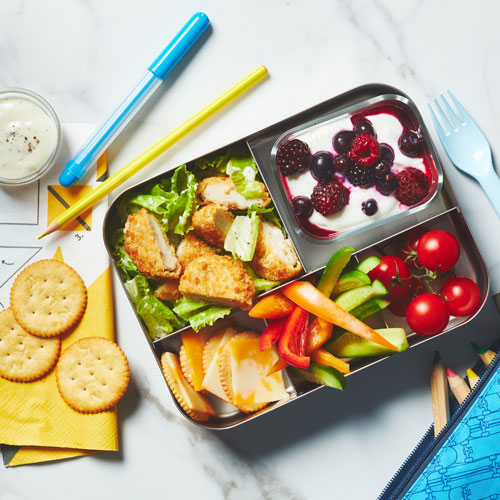  Metal bento box filled with crispy chicken salad, cheese and crackers and yogurt parfait.