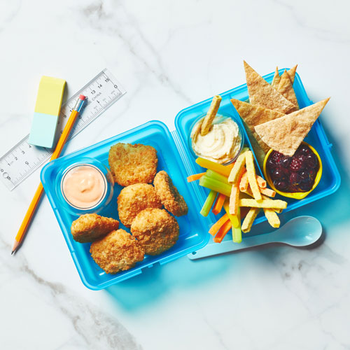 Metal bento box filled with chicken nuggest and dip, veggies, veggie chips and dessert nachos with a fieldberry compote for dipping.