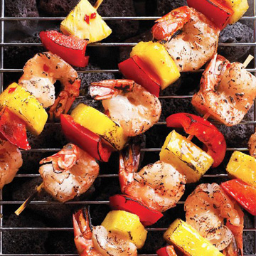 Mandarin ginger shrimp kabobs threaded with red pepper pieces and pineapple on a grill.