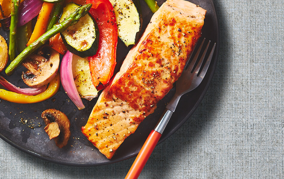 Individual salmon filet on a gray plate with a side of grilled vegetables.