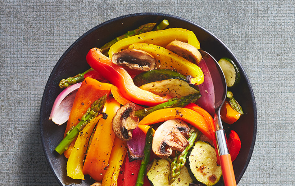 Deluxe mixed vegetable griller in a black bowl with an orange handled spoon.