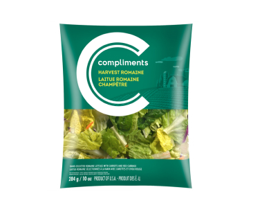  Clear plastic bag of Compliments harvest romaine lettuce with a background of rolling fields and a barn.  

