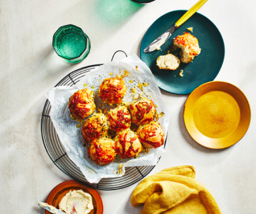 Baked garlic Parmesan cheese pull apart rolls on a wire rack next to a blue plate with one of them buttered on the side. 
