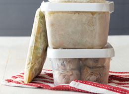 Filled containers and freezer bags of frozen foods with date labels on grey counter.