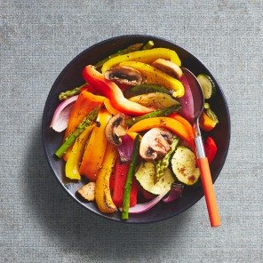 Deluxe mixed vegetable griller in a black bowl with an orange handled spoon.