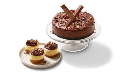 Three mini cheesecakes topped with KitKat spread and pieces sitting on a white plate. 6 inch chocolate cheesecake topped with KitKat spread and bar pieces.