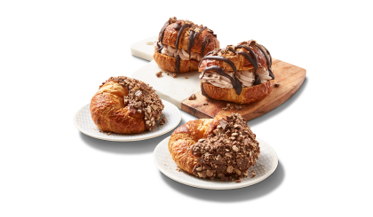 Kit Kat spread and chocolate whip-filled croissants on a white plate. Two croissants, each on its own plate, half covered with KitKat bar chocolate and pieces.