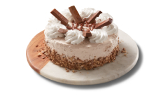 full-triple-layer-cake Chocolate triple layer cake covered in icing and Kit Kat crumbs on the side, topped with chocolate icing, and pieces of the candy bar.
