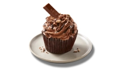 gourmet-cupcakes A single cupcake on a white plate frosted with chocolate icing and garnished with a piece of Kit Kat sticking out of it and candy bar crumbs.