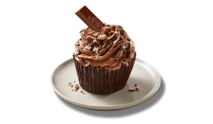 A single cupcake on a white plate frosted with chocolate icing and garnished with a piece of Kit Kat sticking out of it and candy bar crumbs.