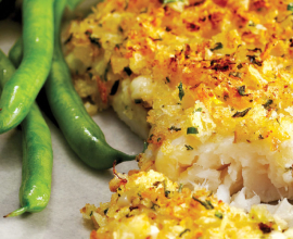 Filet of haddock that’s potato chip crusted served alongside green beans and a slice of lemon on a grey plate.