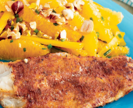 A piece of cod on a blue plate beside a salad of orange slices topped with nuts.