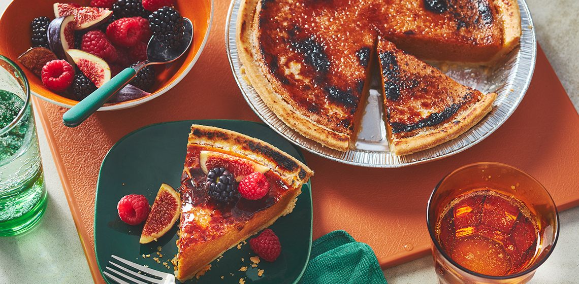 Bruleed pumpkin pie sitting next to a slice garnished with fresh figs, blackberries and raspberries. 