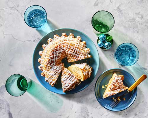 White marble surface with a blue platter topped with a round filled pastry ring, with a white cake server, and a slice cut out.