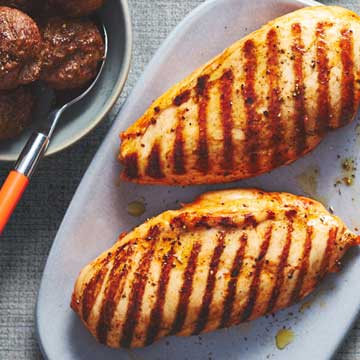 A light blue lavender plate topped with two grilled marinated chicken breasts.