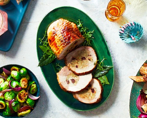 stuffed turkey breast medallions on greeb serving dish with utensils and Brussel sprouts. (TRU: focus on turkey and side dish- NOT prime rib)