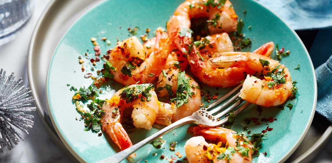 Pile of shrimp scattered on a green plate sprinkled with a chili and orange gremolata.