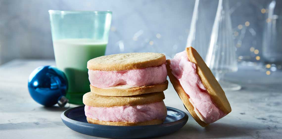 Pink cotton candy sandwiched between two sugar cookies on a blue plate next to a glass of milk.