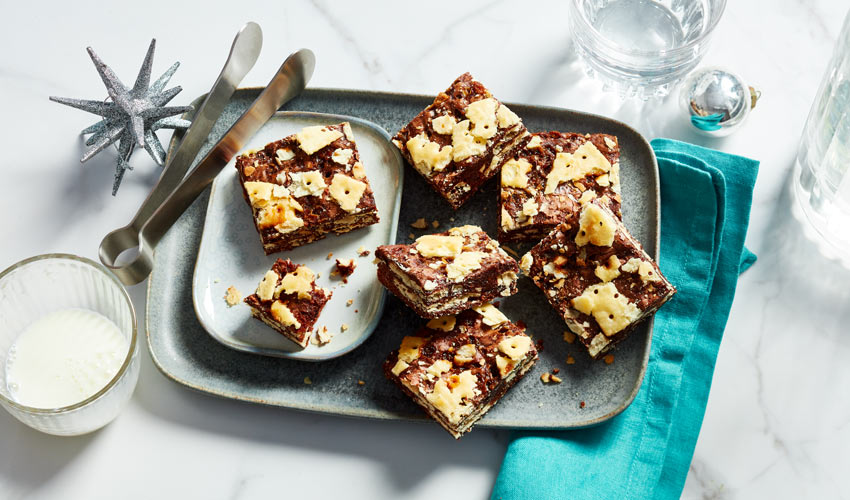 A blue plate of crack brownies topped with bits of saltine crackers next to a glass of milk.