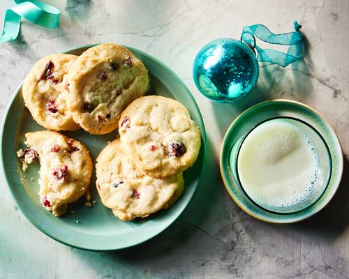 Cranberry white chocolate shortbread cookies on a light green plate next to a glass of cold milk. 