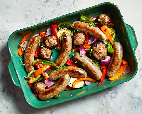 Festive sausages flavoured with apple cranberry stuffing, bacon and caramelized onion in a green baking dish roasted with yellow, green and red bell peppers.