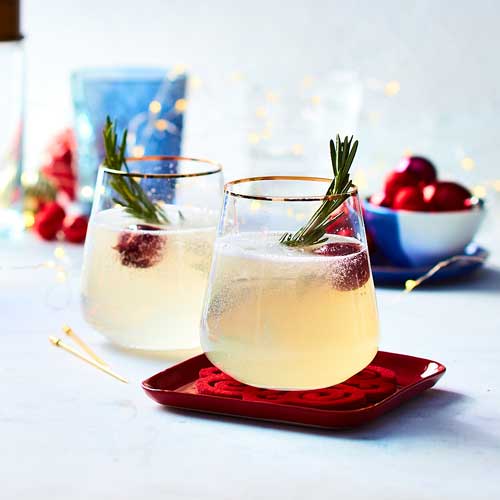 Sparkling martini in gold-rimmed glasses, with a cherry and rosemary garnish in the glass.