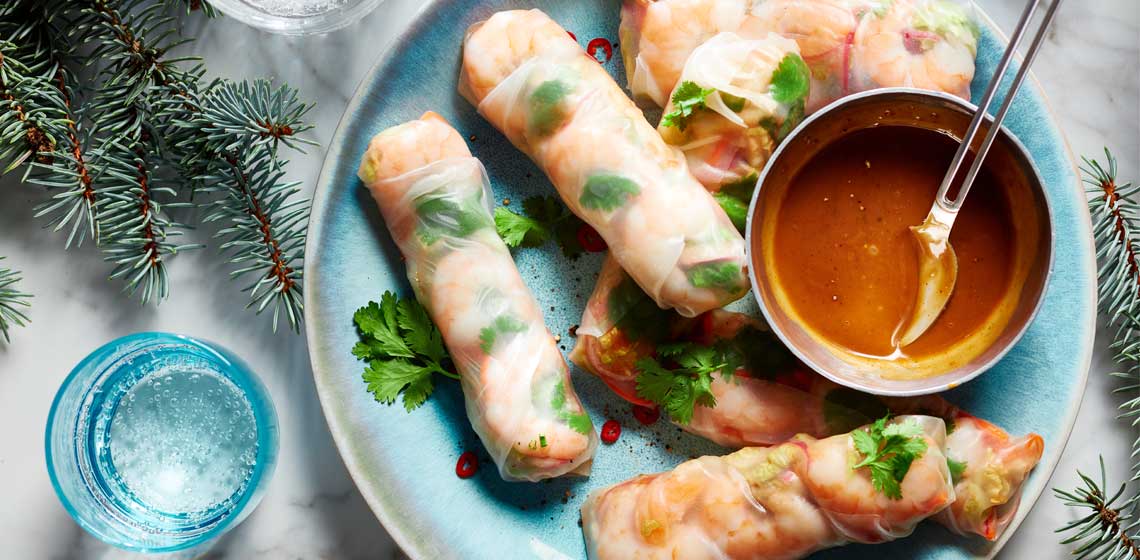 Spring rolls filled with fresh herbs, shrimp, carrots, cabbage and onion on a blue plate.