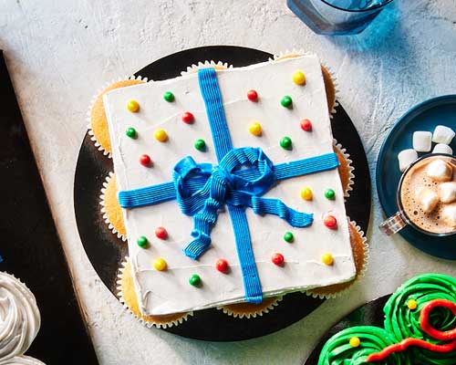 White icing enveloped cupcakes made to look like a gift with a blue ribbon and polka dots