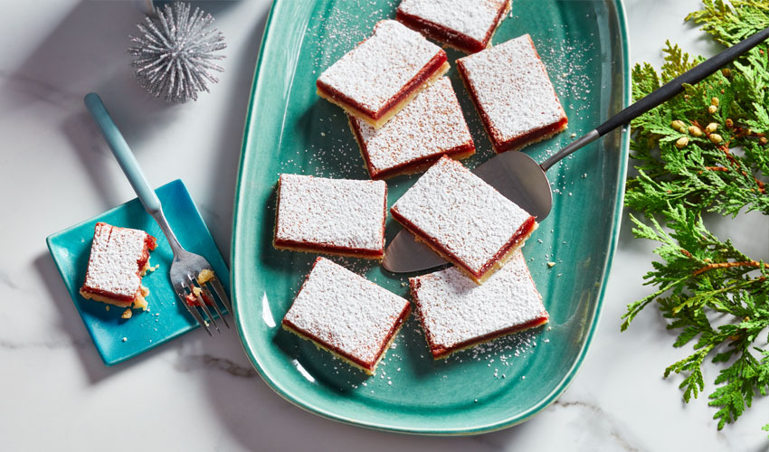 Lemon-cranberry squares cut on a green serving platter next to one on a blue plate.
