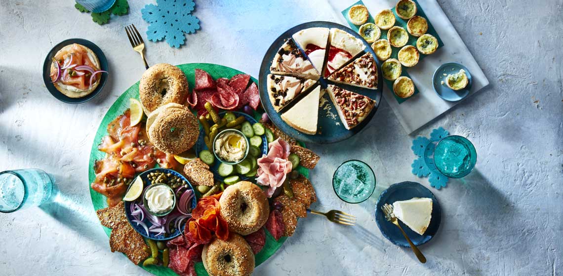Three blue platters full of bagels, smoked salmon, cream cheese, quiches and cheesecake slices.