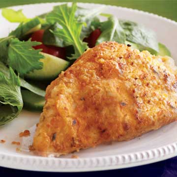 An oven fried chicken breast on a white plate with a side salad. 