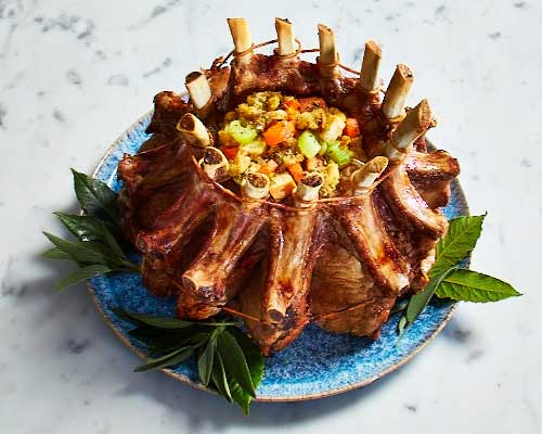 crown roast on plate stuffed with veggies on a blue and white platter.