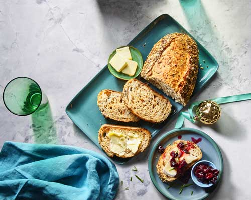 Sliced multigrain harvest load of a blue platter with side plate with jam and butter.