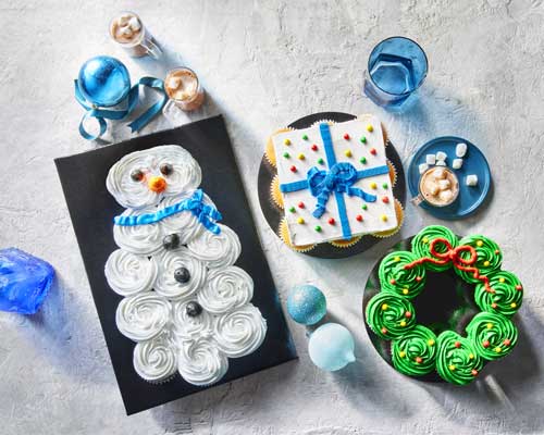 Grey surface with a black plate with a cupcake pull-apart cakes designed in gift, wreath or snowman using icing on top to connect the cupcakes.