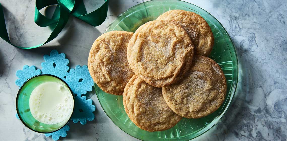 Cinnamon sugar topped snickerdoodle cookies on a blue plate next to a glass of milk.