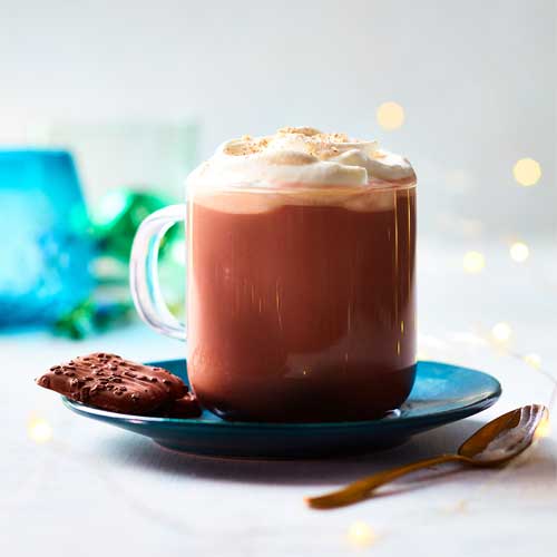 A glass mug filled with spiked hot chocolate with dark rum and salted caramel, topped with whipped cream.